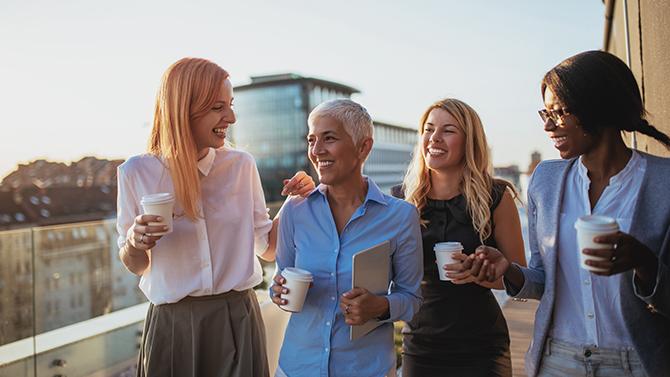 CoT-HW-4 female professionals with coffee laughing together on balcony with buildings in the background