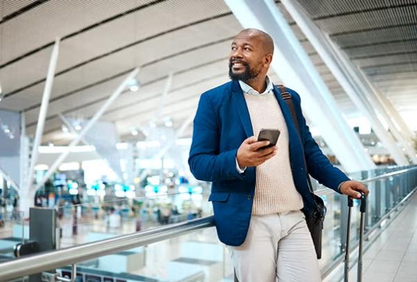 Man holding phone in an airport demonstrating the importance of business travel management.