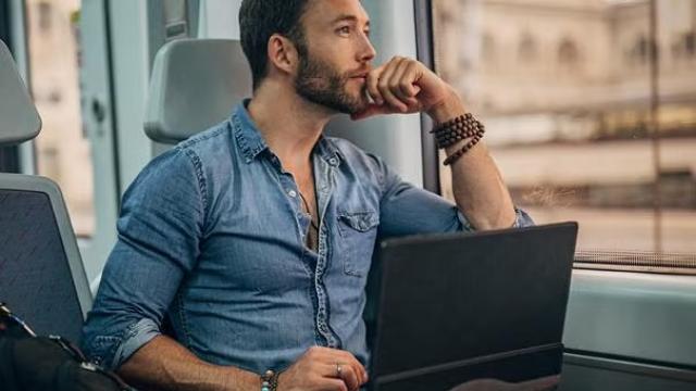 Man sitting on a train with a laptop on his lap and enjoying the bleisure trend