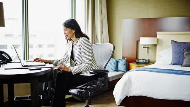 A woman sitting on the desk with a laptop in her hotel room showcasing the most in-demand hotel amenities