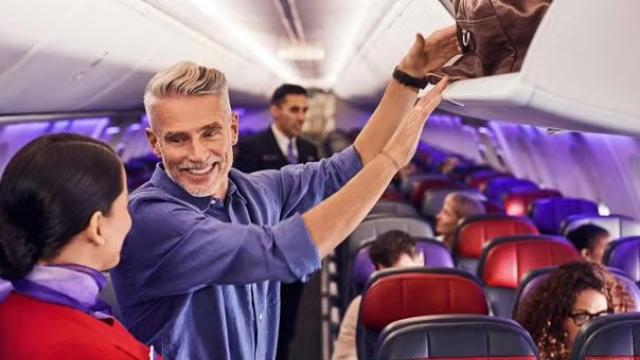 Man talking to flight attendant while putting luggage in the overhead compartment representing Velocity Frequent Flyer points.