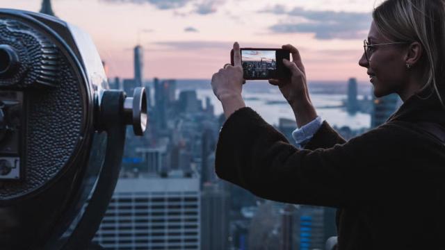 Woman taking a picture of the New York skyline representing the top international business flight destinations