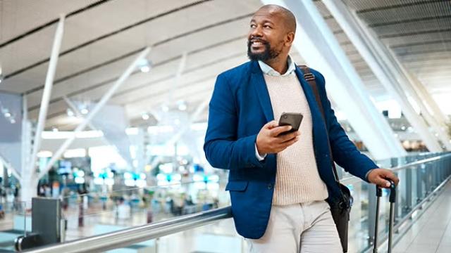 Man holding phone in an airport demonstrating the importance of business travel management.