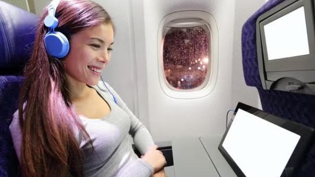 Woman enjoying a movie on a tablet on a flight representing inflight airline entertainment. 