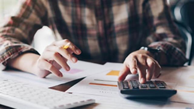 Man working on a calculator surrounded by books, representing Flight Centre Travel Group upgrade of its profit guidance
