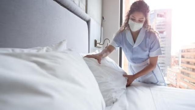 Hotel worker making the bed demonstrating how to survive hotel quarantine. 