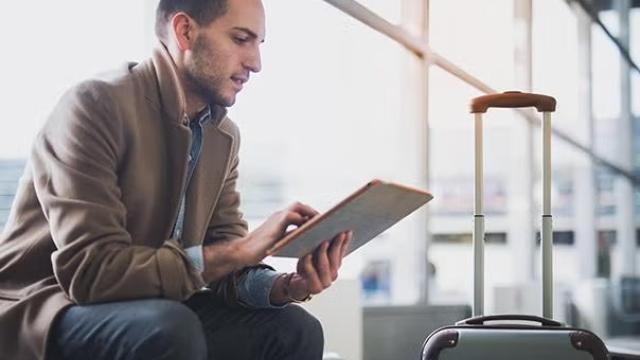 Man looking at a tablet sitting in the airport representing a specific business traveller type. 