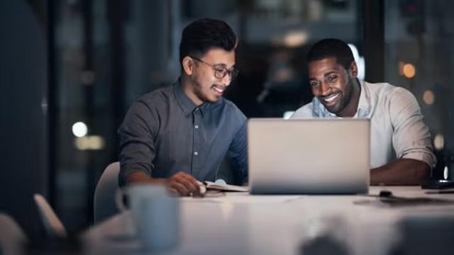 Two men talking over a laptop representing the importance of collaboration. 
