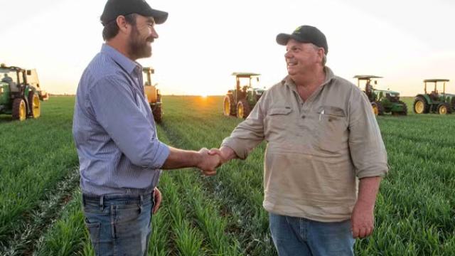 Two men shaking hands with farming machinery in the background representing how RDO Equipment’s travel needs were met by the right TMC. 