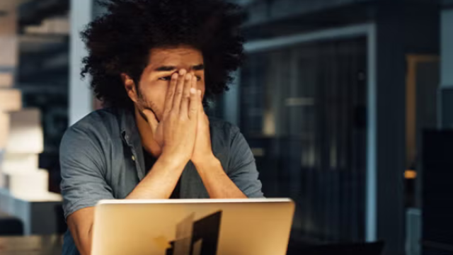 Man sitting in front of laptop with hands on face looking frustrated representing why DIY travel bookings are bad for business.
