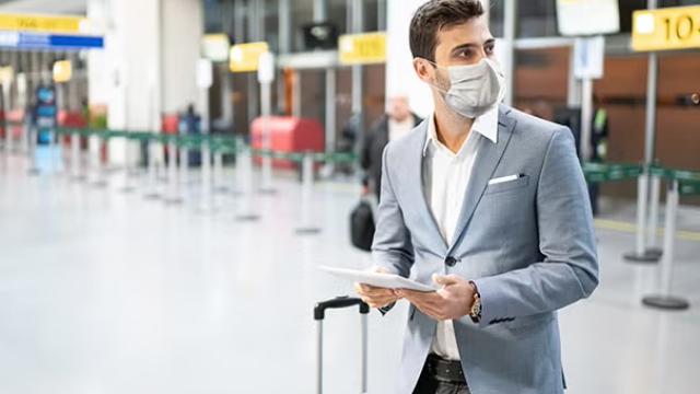 Man walking in the airport holding a tablet representing the pros and cons of unmanaged travel versus a managed travel.