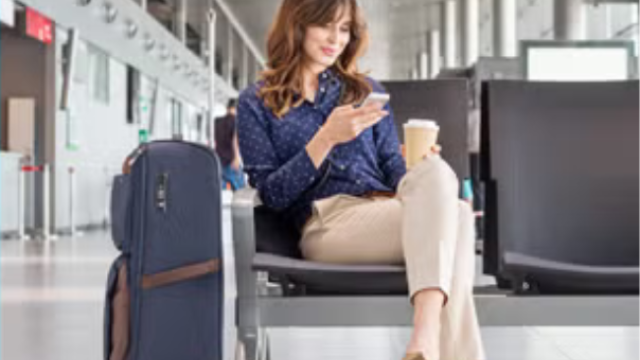 A woman sitting in the airport next to her suitcase representing the importance of sustainability in business travel. 