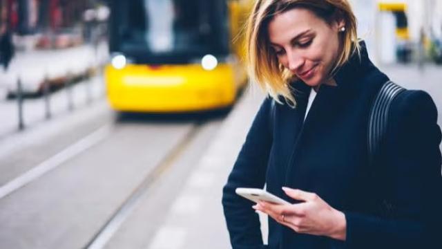  Woman waiting for the train while using a smartphone representing the best apps for travel preparation.