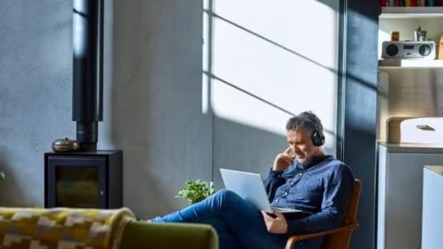 Man sitting on a chair looking at laptop and wearing earphones representing 9 critical questions you need to be asking your travel management company right now.