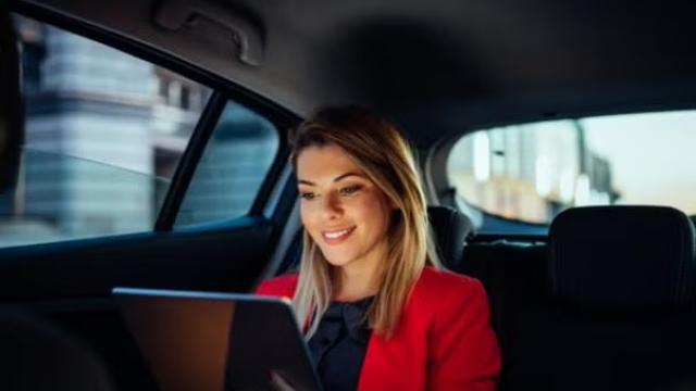 A woman sitting in the backseat of a car holding a tablet representing the sharing economy trend.