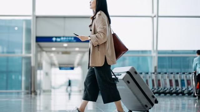 A woman pushing a suitcase through the airport, highlighting the importance of cost-saving tactics used by savvy business travellers.