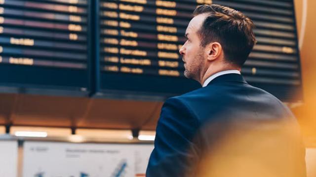 Man looking at information board at the airport demonstrating changes in international airfares in corporate travel