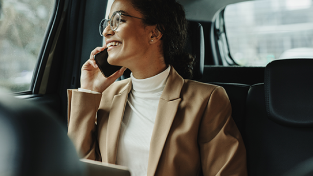 Woman speaking on the phone while sitting at the back of a car demonstrating how to create an effective employee travel safety policy to enhance risk management.