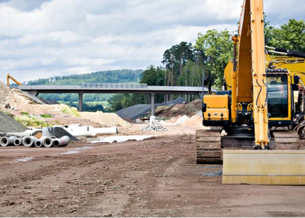 Road construction site with digger in foreground and bridge in background