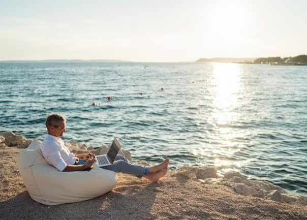 Man working on the laptop on the beach representing the bleisure travel trend.