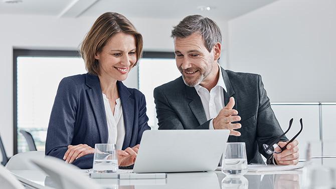 Man and woman smiling in a meeting looking at a computer screen.