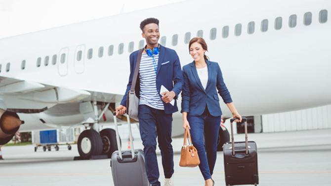 Man and woman walking across tarmac in front of a plane.