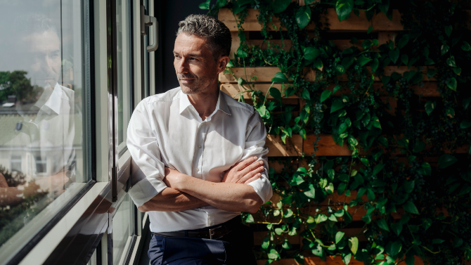 Man standing near green wall looking out of window.