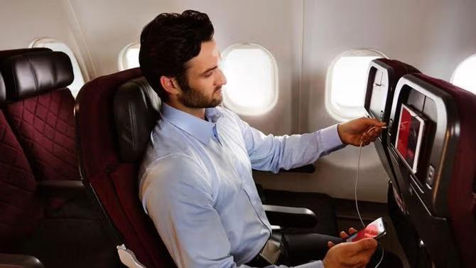 Man plugging in earphones jack into a airplane tv screen representing inflight airline entertainment. 