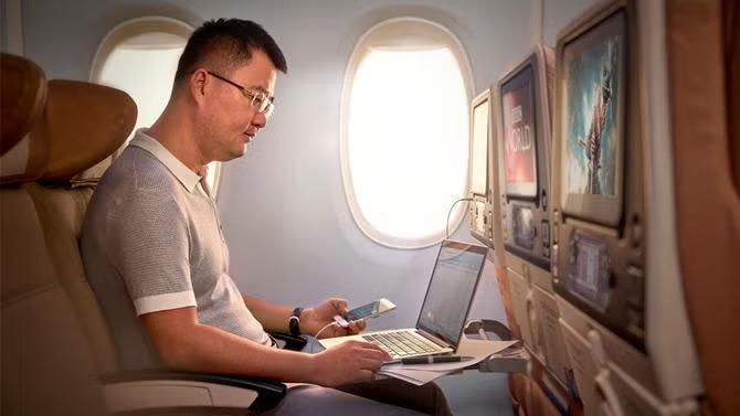 Man looking at laptop on an airplane representing inflight airline entertainment. 
