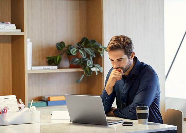 Man thinking at desk while working on laptop.