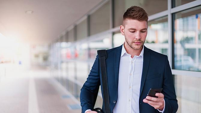 A man walking outside an airport, looking at his phone, using YOUR.CT travel manager tech portal for easy business travel management.