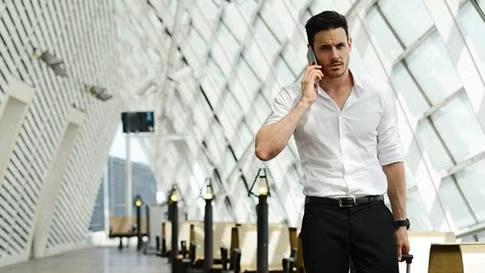Man speaking on the phone while in walking through the airport representing a specific business traveller type. 