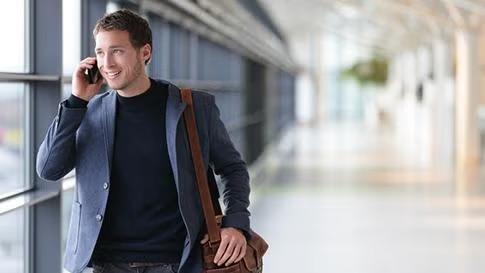 Man speaking on the phone walking a hallway representing a certain business traveller type. 