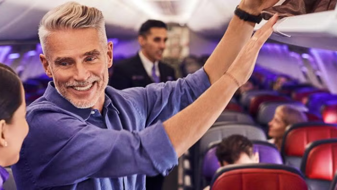 Man talking to flight attendant while putting luggage in the overhead compartment representing Velocity Frequent Flyer points.