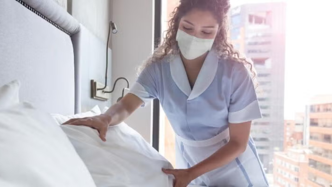 Hotel worker making the bed emonstrating how to survive a hotel quarantine. 