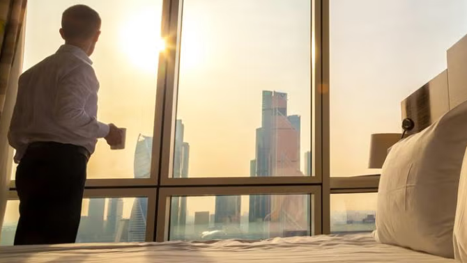 Man looking at city view from hotel room representing the best option for your hotel rates.