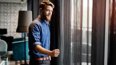Man opening the curtain in a hotel room, demonstrating a business traveller's guide to London.