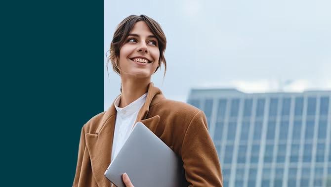 Woman holding laptop standing outside representing the importance of elevating your company’s travel program.