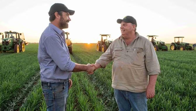 Two men shaking hands with farming machinery in the back representing how RDO Equipment’s travel needs were met by the right TMC. 