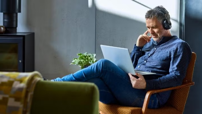 Man sitting on a chair looking at laptop and wearing earphones representing 9 critical questions you need to be asking your travel management company right now.
