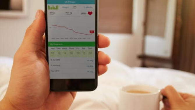 Hand holding a smartphone in bed representing the best apps for travel preparation.