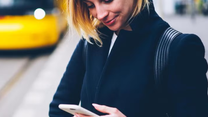 Woman waiting for the train while using smartphone representing the best apps for travel preparation.