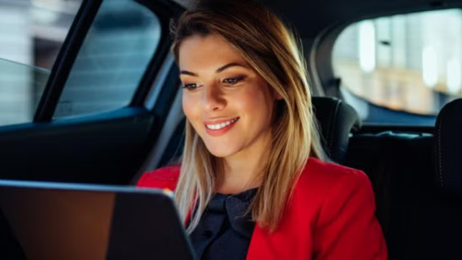 Woman sitting in the backseat of a car looking at a tablet representing the sharing economy trend.