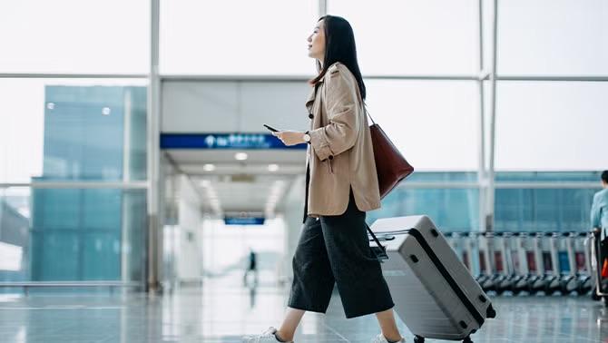 A woman pushing a suitcase through the airport, highlighting the importance of cost-saving tactics used by savvy business travellers.