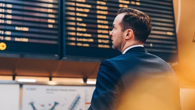 Man looking at information board at the airport demonstrating changes in international airfares in corporate travel