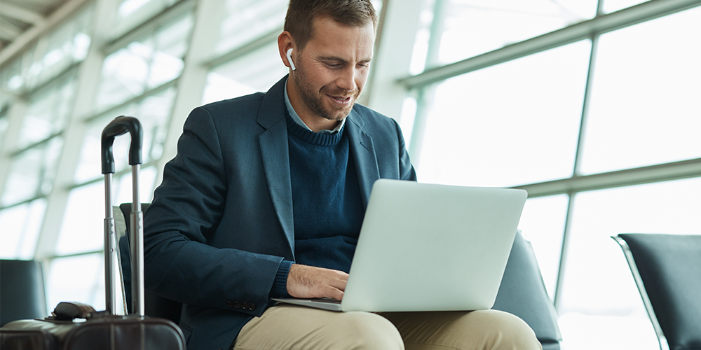 Man working on a laptop while seated in an airport representing how Corporate Traveller delivers technology and expense solutions that allow you to manage your travel, get vital information about your travel patterns and stay in control of your travel expenses.