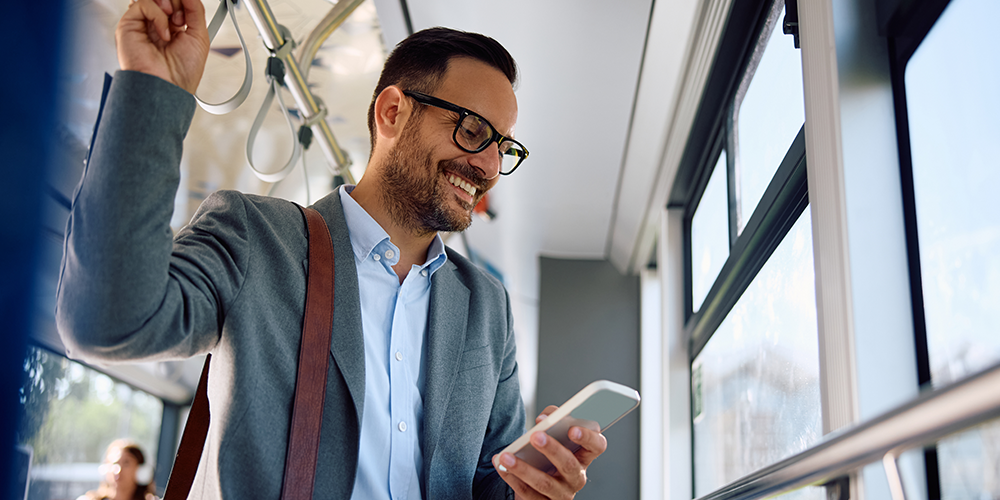 Man looking at smartphone while standing in an airport bus representing how Corporate Traveller delivers technology and expense solutions that allow you to manage your travel, get vital information about your travel patterns and stay in control of your travel expenses.