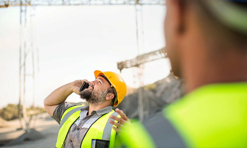 Man on construction site talking on the phone representing how travellers get an extra layer of traveller security with Safe & Secure. 