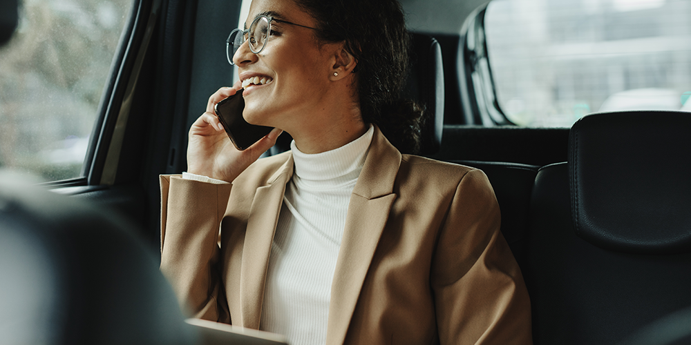 Woman speaking on the phone while sitting at the back of a car demonstrating how to create an effective employee travel safety policy to enhance risk management.
