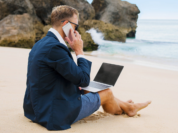 Man sitting on a beach using a laptop enjoying the flexibility and convenience of business travel tech tools